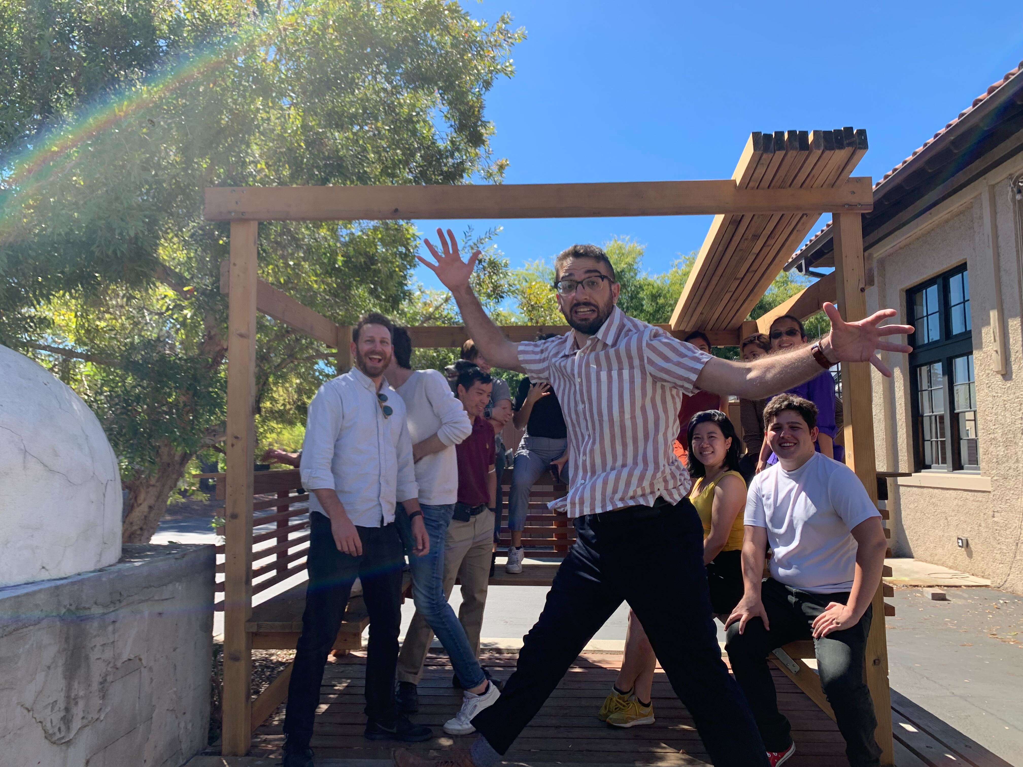 the lab outside smiling inside of the pergola, eric jumping in front of everyone with a smile on his face