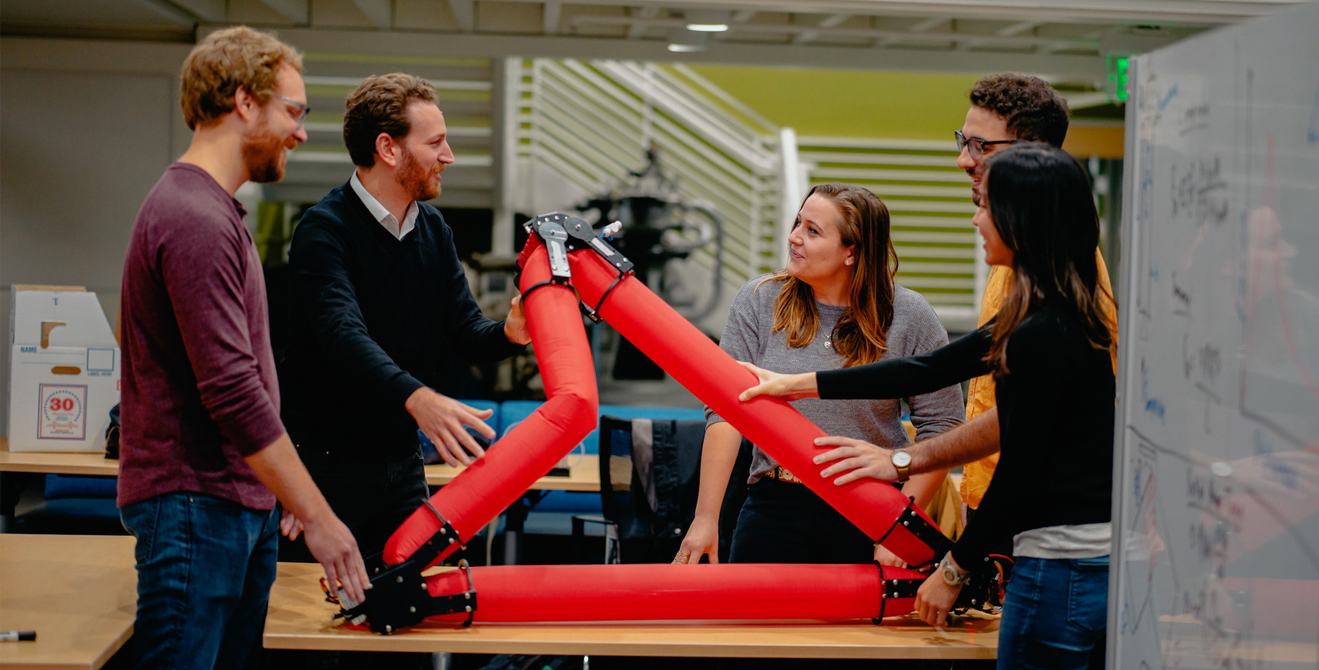 Image of 5 people engaged in discussion and gathered around a pneumatic truss robot
